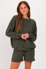woman wearing an olive green long sleeve sweatshirt and matching shorts, smiling and posing against a plain background