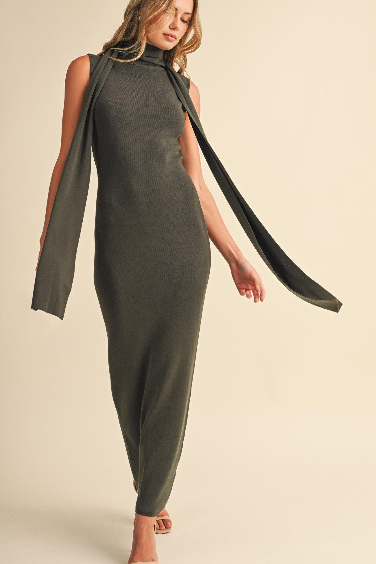 woman wearing a form-fitting olive green sleeveless maxi dress with a scarf detail