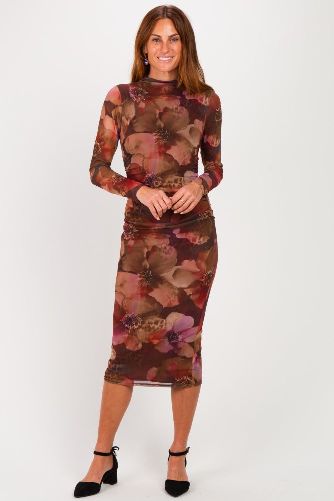 woman wearing a floral long sleeve midi dress in warm tones with ruched detailing and black heels