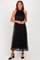 woman wearing a black halter neck midi dress with sequin details and a sheer overlay, styled with black heels
