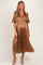 woman wearing a brown pleated maternity dress with short sleeves and a wrapped bodice, showcasing her baby bump