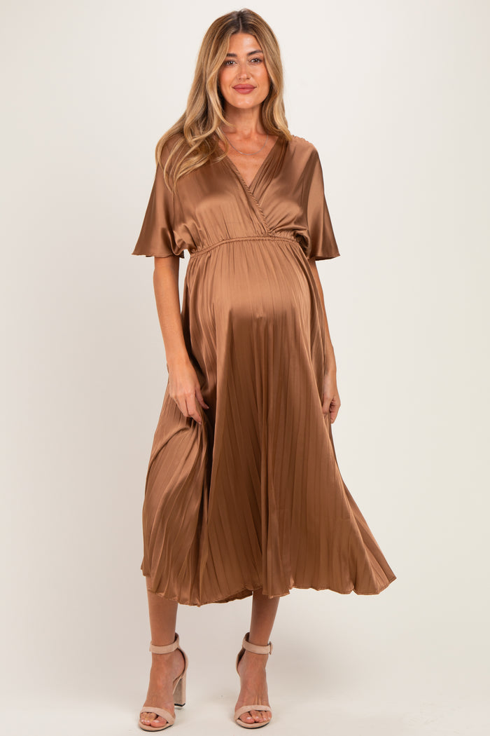 woman wearing a brown pleated maternity dress with short sleeves and a wrapped bodice, showcasing her baby bump