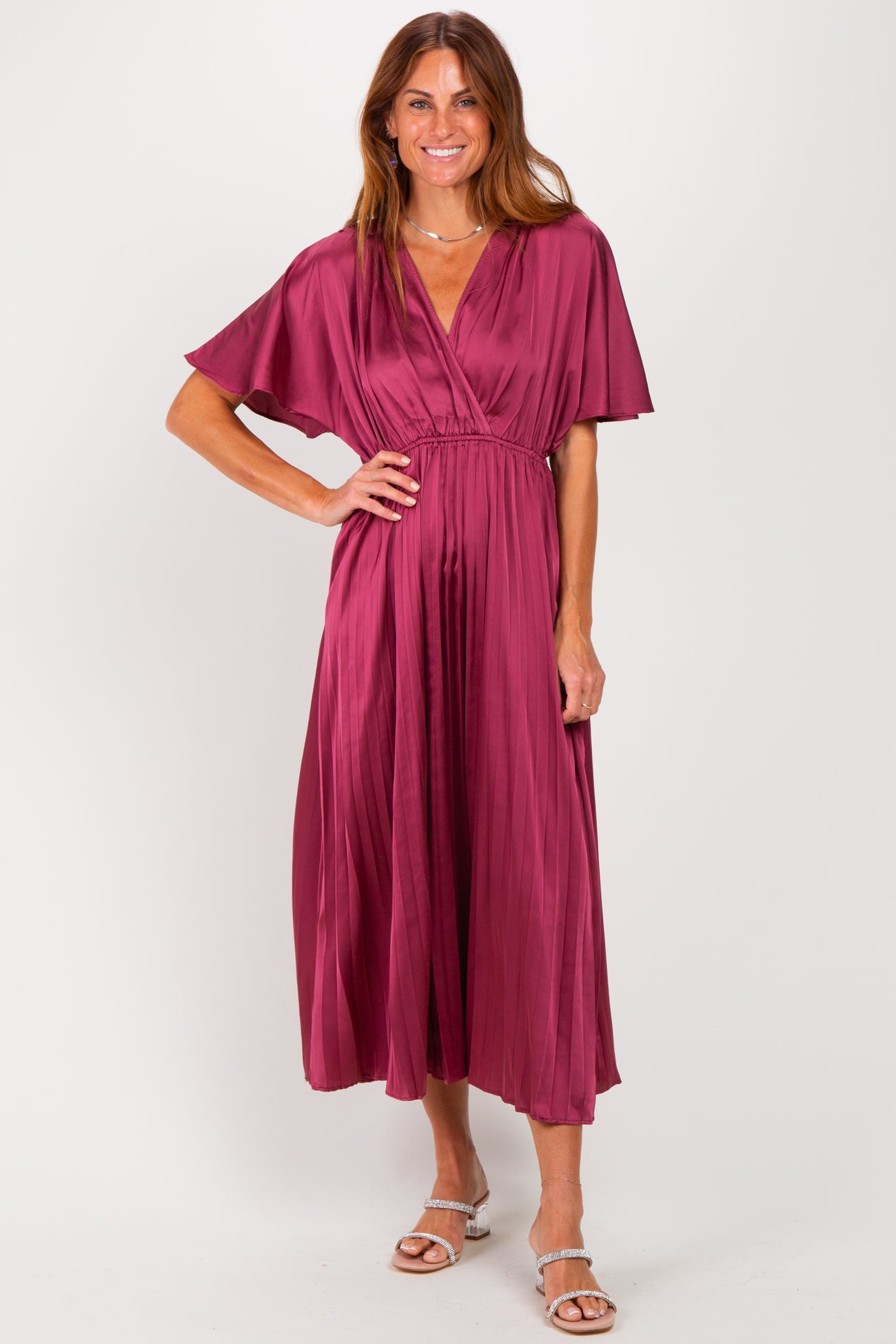 woman wearing a burgundy pleated maxi dress with flutter sleeves and a tie at the waist