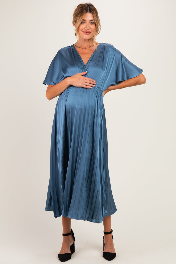 woman wearing a teal pleated maternity dress with flutter sleeves and holding her baby bump