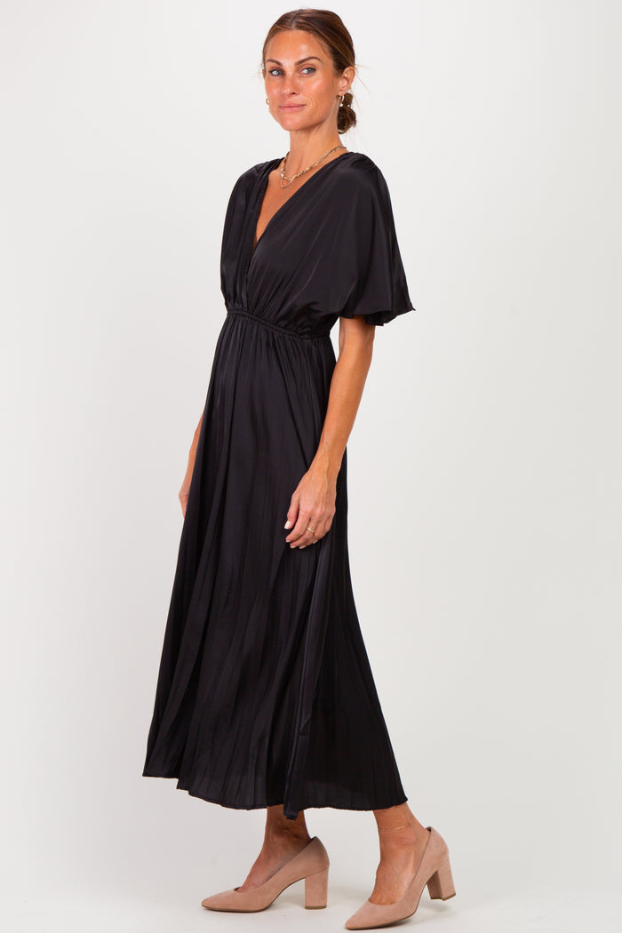woman wearing a black pleated maxi dress with a deep V-neck and short sleeves, standing in profile