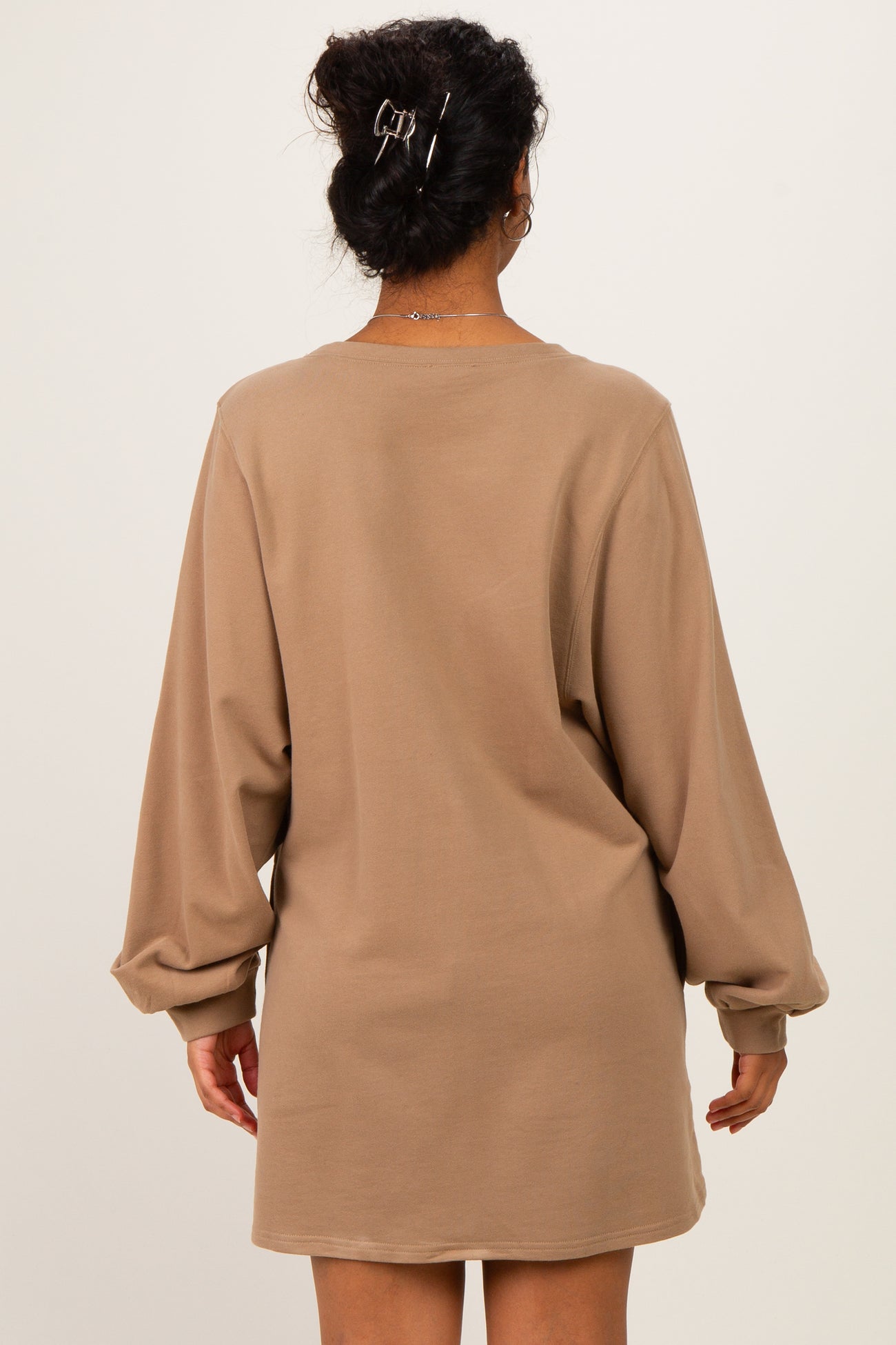woman wearing a beige long sleeve maternity dress, showing a relaxed fit and loose sleeves from the back