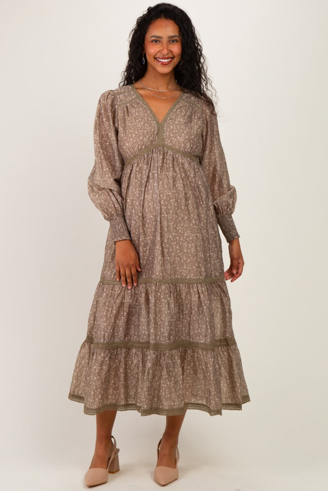 woman wearing a brown floral print maternity maxi dress with long sleeves and a tiered skirt, showcasing her baby bump