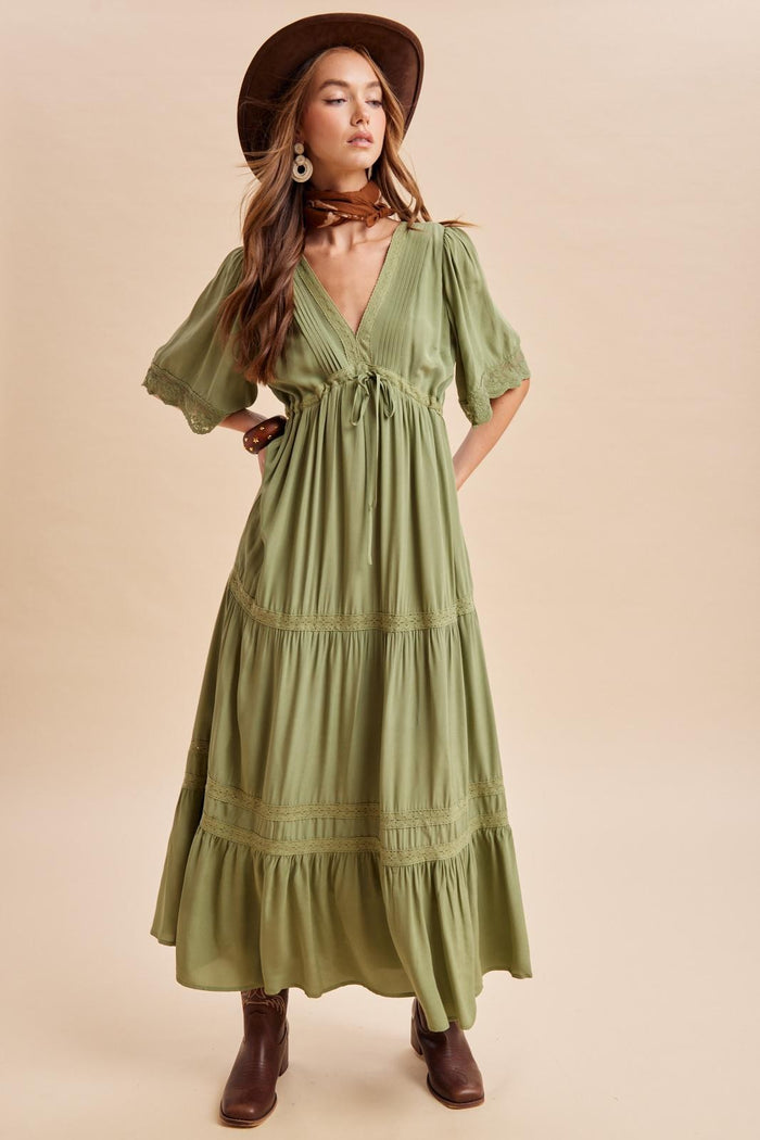woman wearing a green maxi dress with puff sleeves and a tie front, styled with a wide-brim hat and brown ankle boots