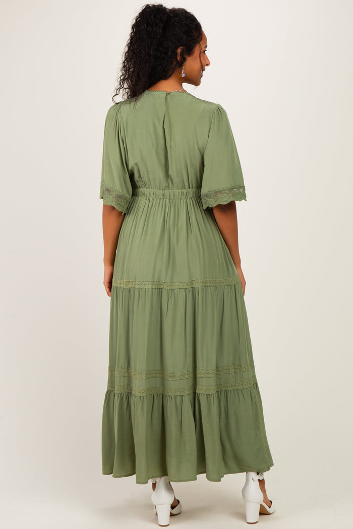 woman wearing a long green maternity dress with lace details and a tiered skirt, showing her baby bump from the back
