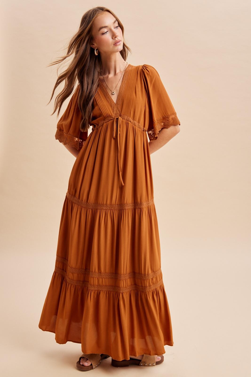 woman wearing an orange maxi dress with a v-neck, flutter sleeves, and tiered ruffle details