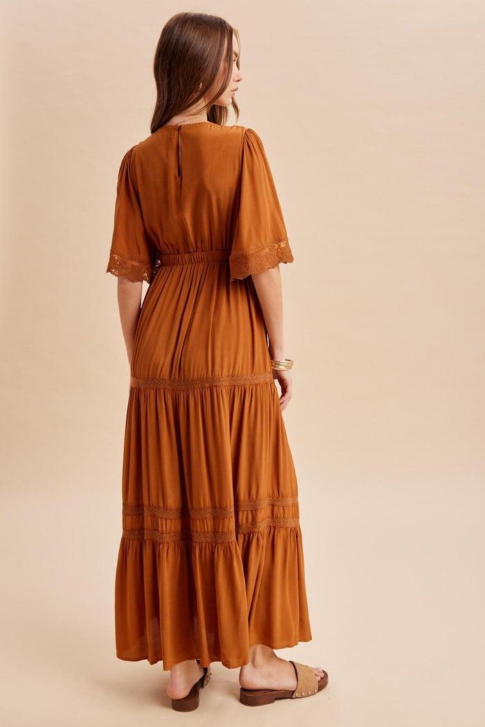 woman wearing a rust-colored maxi dress with lace details and a tiered hem, viewed from the back
