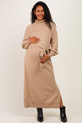 woman wearing a tan maternity sweater dress with a tie waist and long sleeves, showing her baby bump