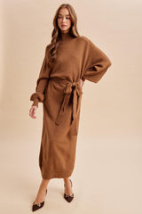woman wearing a brown long sleeve knit dress with a tie waist and ribbed hem, styled with brown heels