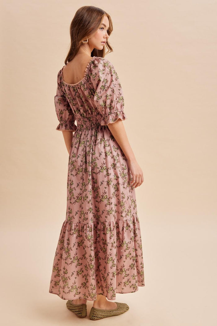 woman wearing a pink floral maxi dress with puff sleeves and a tiered skirt, standing with her back to the camera