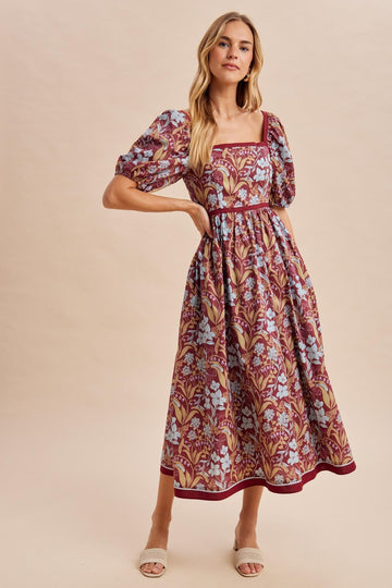 woman wearing a maroon floral midi dress with puff sleeves and a square neckline, standing in a relaxed pose