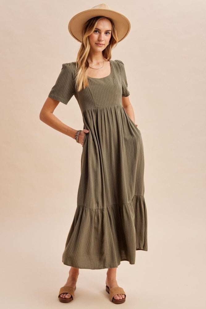 woman wearing a short sleeve olive green maxi dress with pockets and a tiered skirt, styled with a wide-brim hat