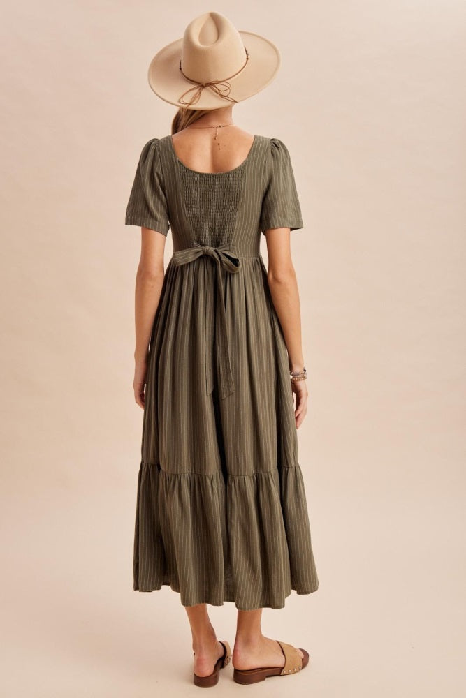 woman wearing an olive green midi dress with short puff sleeves and a tie belt, standing with her back to the camera