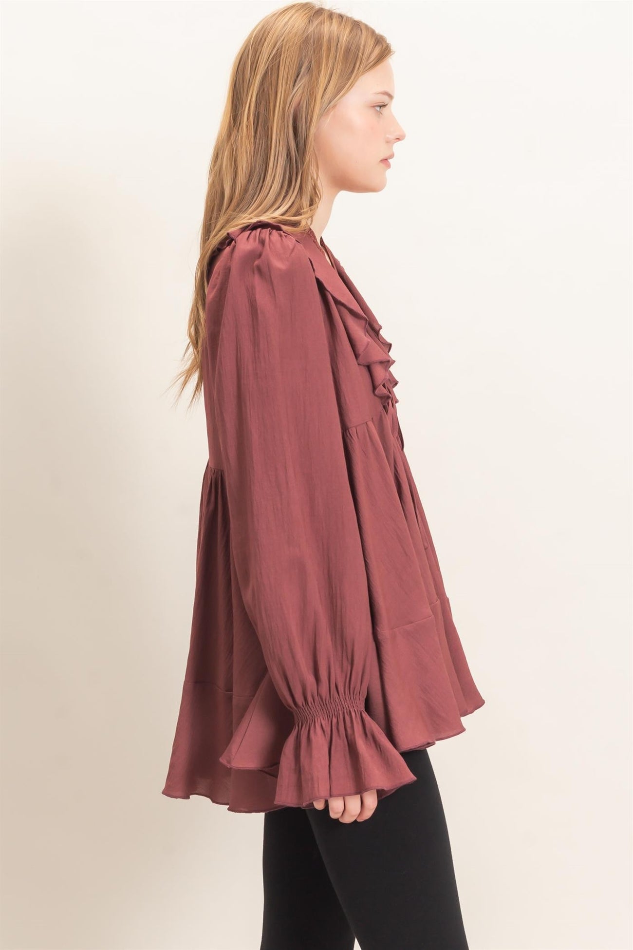 woman wearing a burgundy ruffled blouse with bell sleeves and a relaxed fit, paired with black leggings