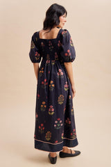 woman wearing a black floral maxi dress with puff sleeves and a smocked bodice, standing with her back to the camera