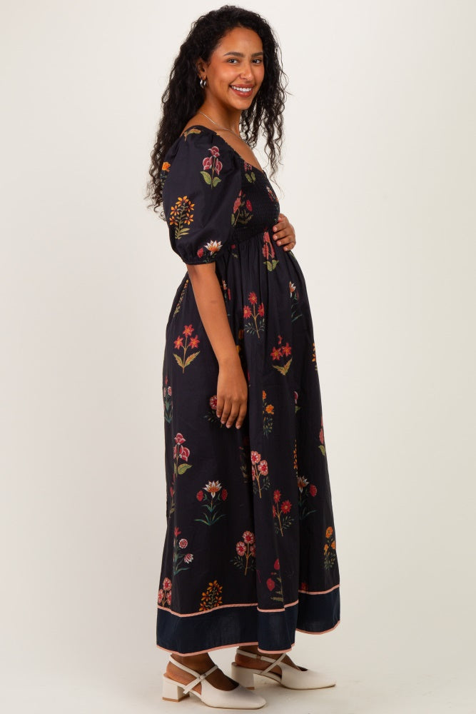 woman wearing a black floral maternity maxi dress and showing her baby bump