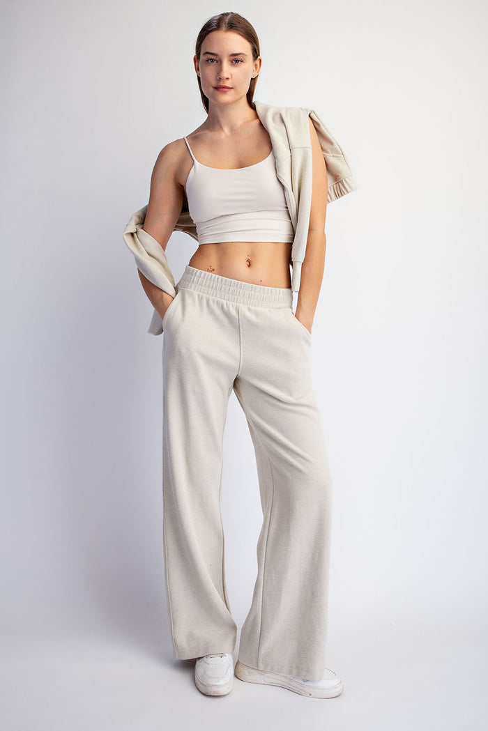 woman wearing a light beige cropped tank top and matching wide-leg pants, holding a sweater over her shoulder