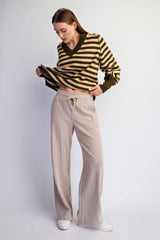 woman wearing a striped brown and olive green cropped sweater and beige wide-leg pants, looking down at her outfit
