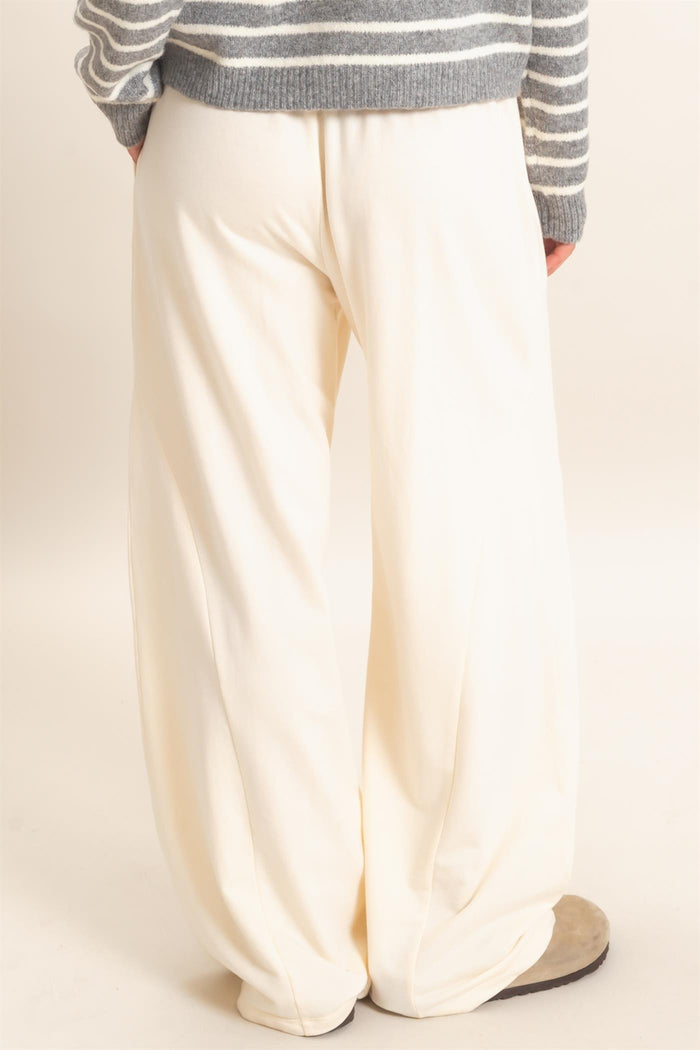 woman wearing white wide-leg pants, standing with her back to the camera, paired with a gray striped sweater