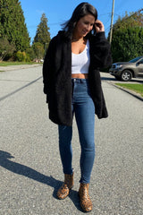 woman wearing a black fuzzy oversized cardigan, white tank top, high-waisted jeans, and leopard print ankle boots