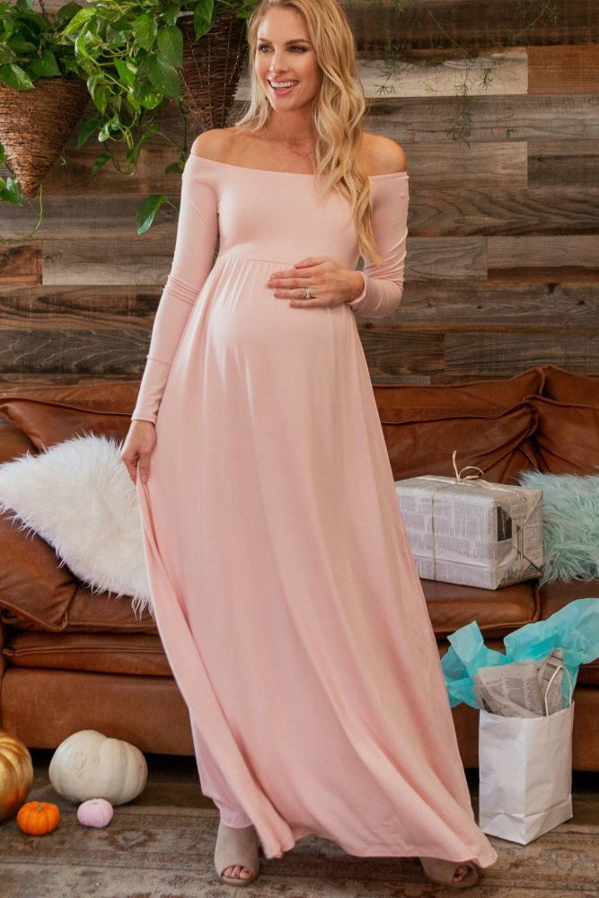 woman wearing a blush pink off-shoulder maternity maxi dress and holding her baby bump