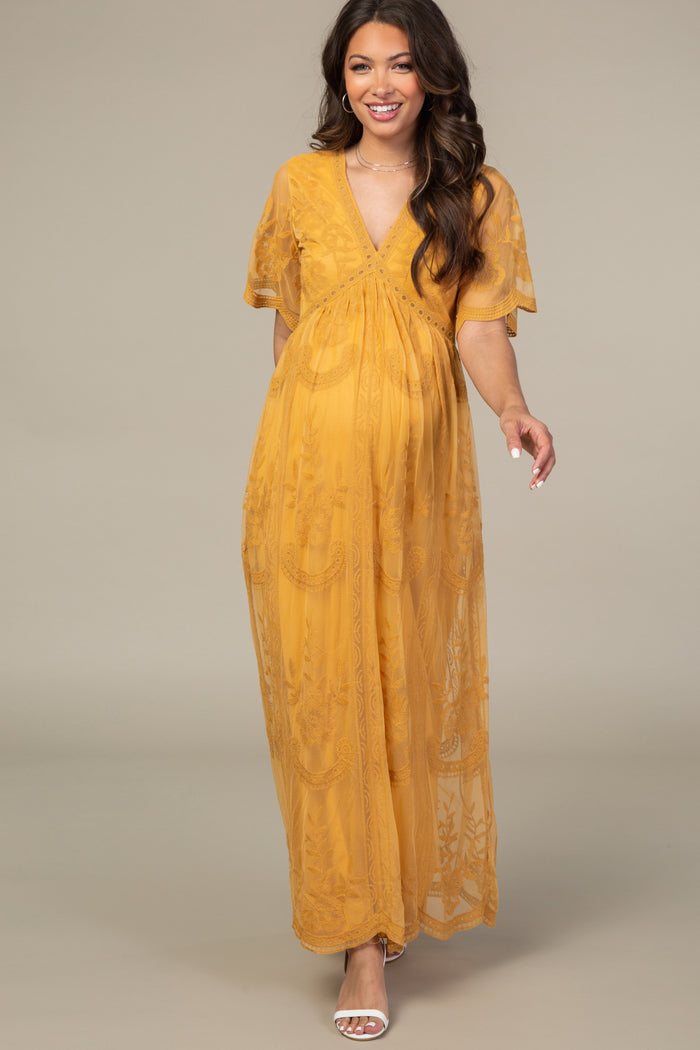 woman wearing a mustard yellow maternity maxi dress with short sleeves and floral lace detailing, showcasing her baby bump