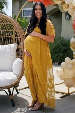 woman wearing a mustard yellow maternity dress with a lace overlay, gently cradling her baby bump