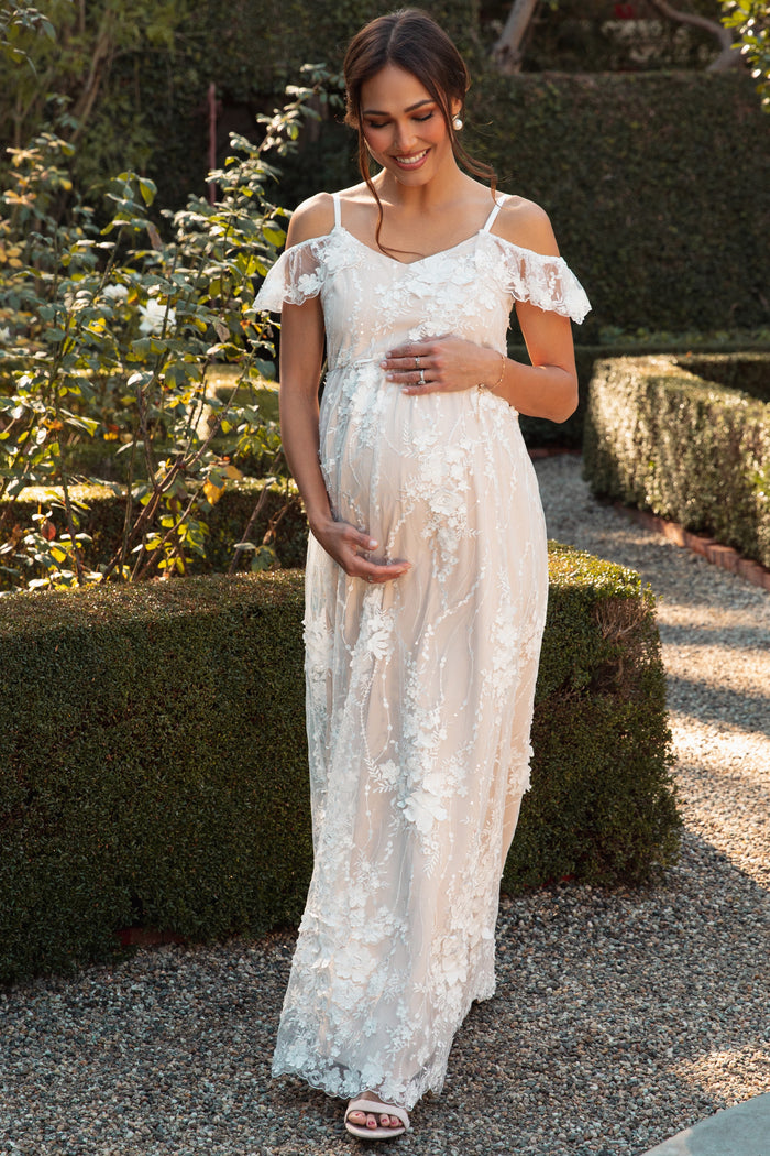 pregnant woman in white floral lace maternity dress holding a bouquet of pink roses