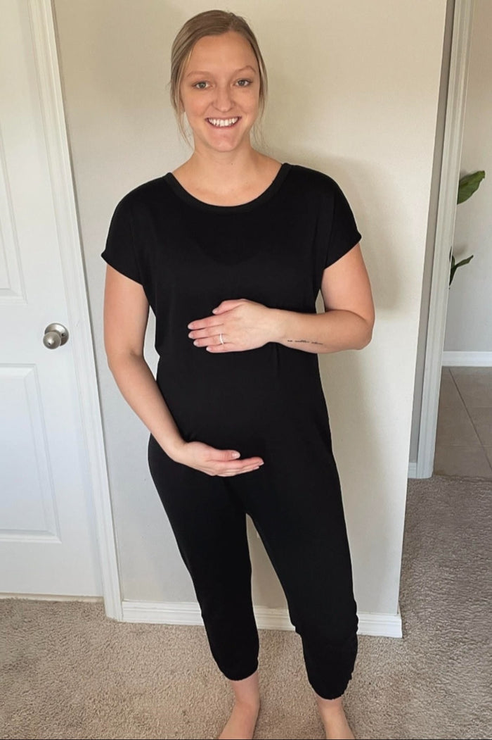 woman wearing a black short sleeve maternity jumpsuit and holding her baby bump