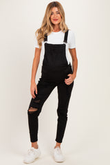 woman wearing black maternity overalls with distressed details and a white fitted top, no visible baby bump