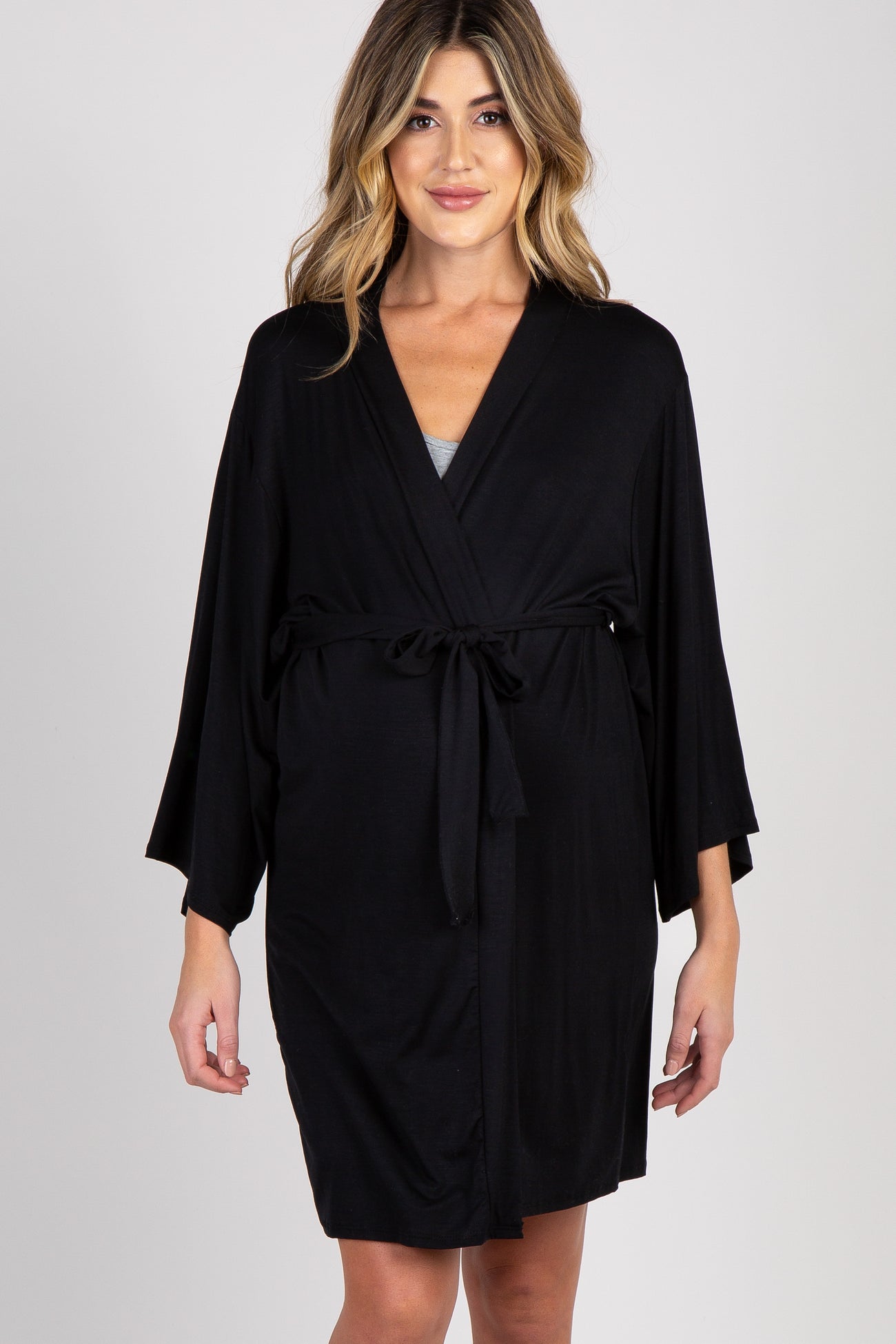 woman wearing a dark brown maternity robe, smiling and holding her baby bump, standing near a fireplace