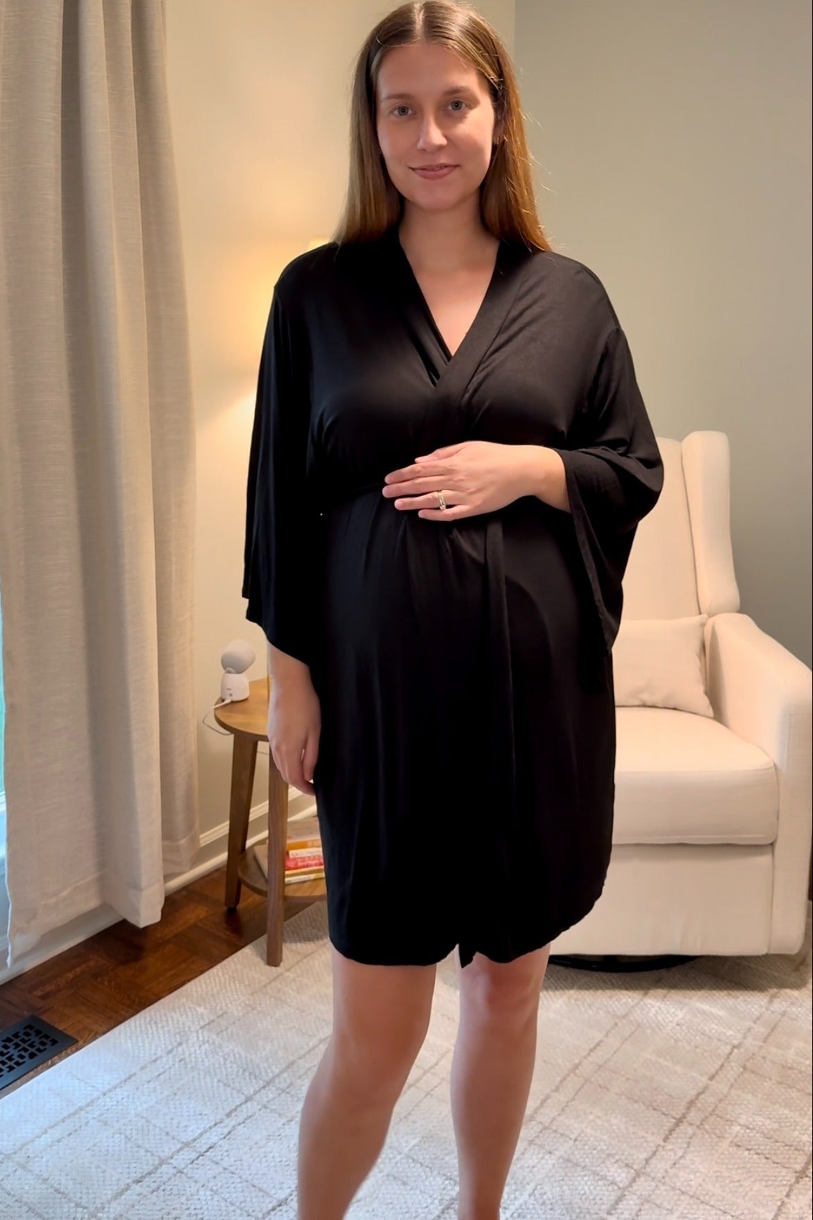 woman wearing a black maternity robe and holding her baby bump in a living room setting