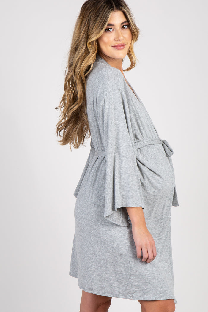 woman wearing a light gray maternity wrap dress, showcasing her baby bump while smiling and posing elegantly
