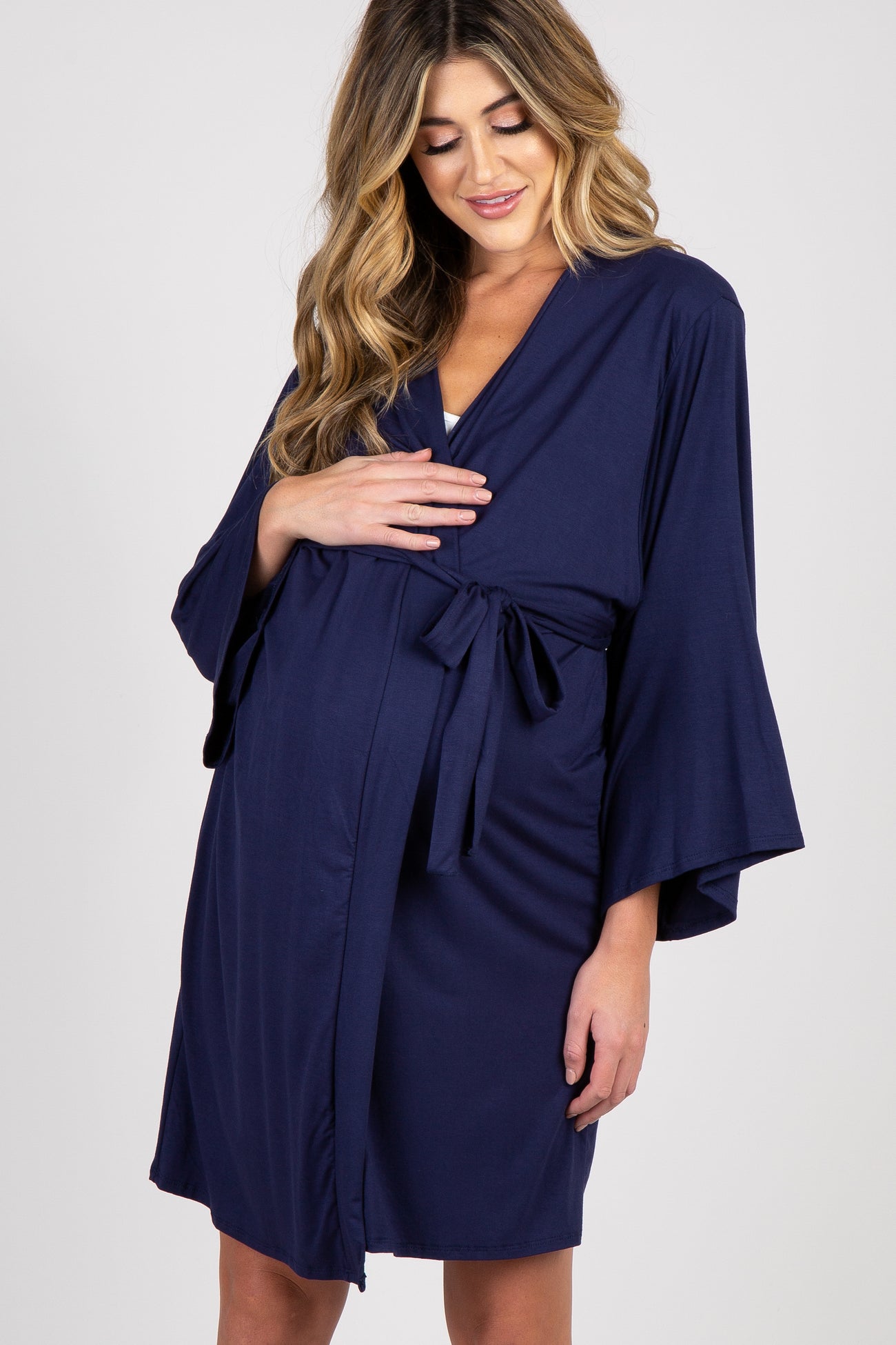 woman wearing a navy blue maternity robe and cradling her baby bump while kneeling on a bed