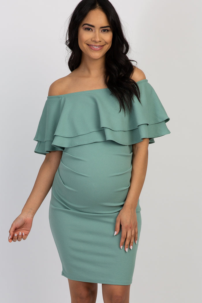 woman wearing a mint green off-shoulder ruffled maternity dress with a visible baby bump