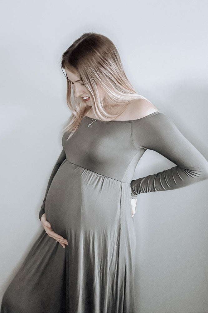 woman wearing an olive green off-the-shoulder maternity dress and cradling her baby bump