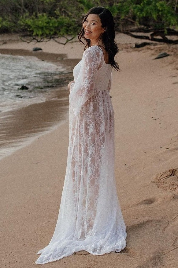 woman wearing a white lace maternity gown standing on the beach, showcasing a visible baby bump