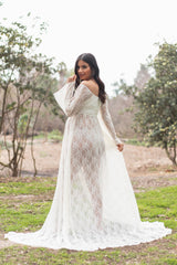woman wearing a sheer white lace maternity gown with long sleeves and a flowing train, showcasing her baby bump