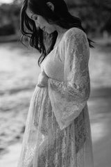 woman wearing a sheer lace maternity robe, holding her baby bump by the water