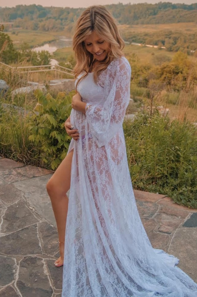 woman wearing a sheer white lace maternity robe and holding her baby bump while standing outdoors