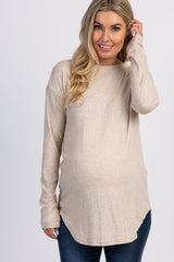 woman wearing a light beige long sleeve maternity top with a rounded hem and a visible baby bump