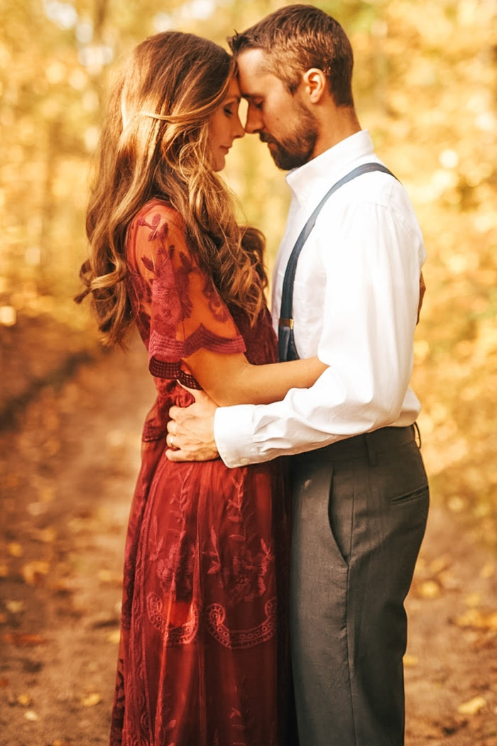 woman wearing a burgundy lace and chiffon maxi dress with short sleeves, standing closely with a man in a white shirt and suspenders