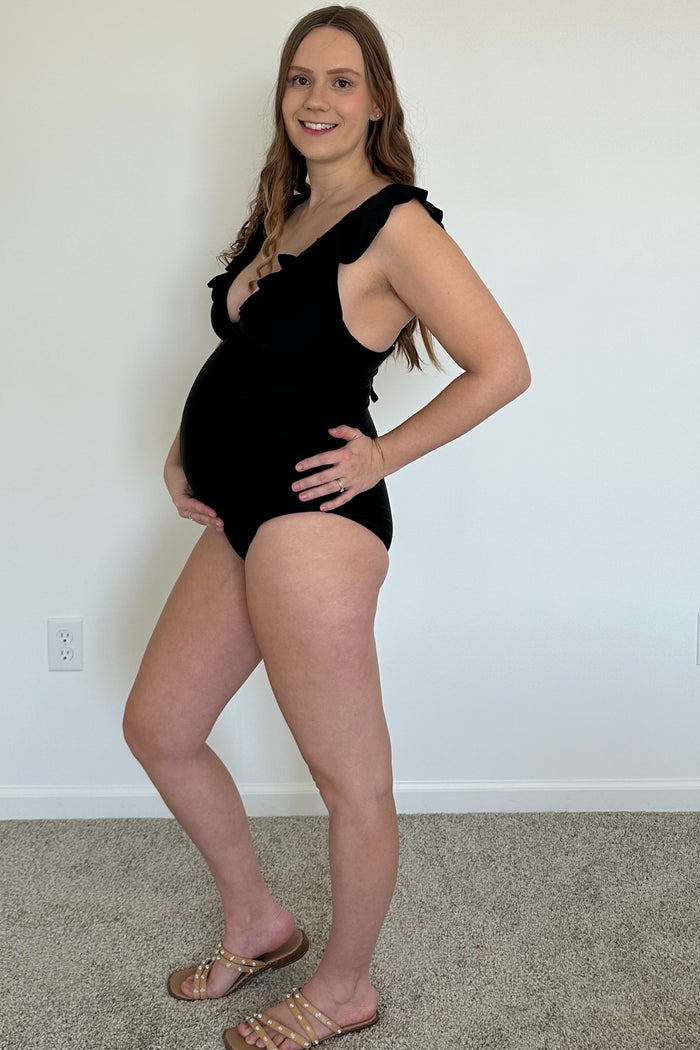 woman wearing a black ruffled maternity swimsuit and showing her baby bump