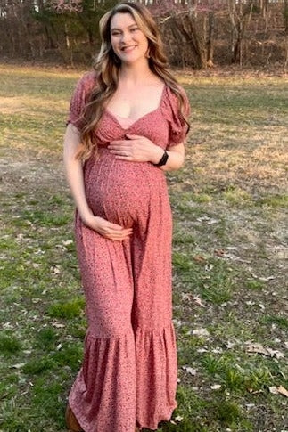 woman wearing a pink floral maternity dress, smiling and holding her baby bump in an outdoor setting