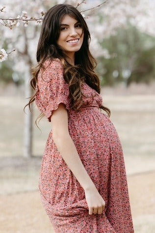 woman wearing a floral pink maternity dress and showing her baby bump outdoors