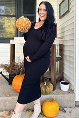 woman wearing a black ribbed long sleeve maternity dress and holding a pumpkin, showcasing her baby bump